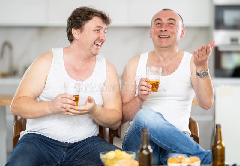 Two adult male friends drinking beer and eating chips at home. Bad habits, eating disorder, alcoholism