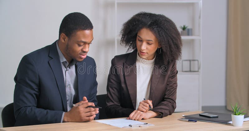 Two Afro American business partners couple of ethnic people sitting at table reading document woman advisor lawyer. Consultant showing to employee contract