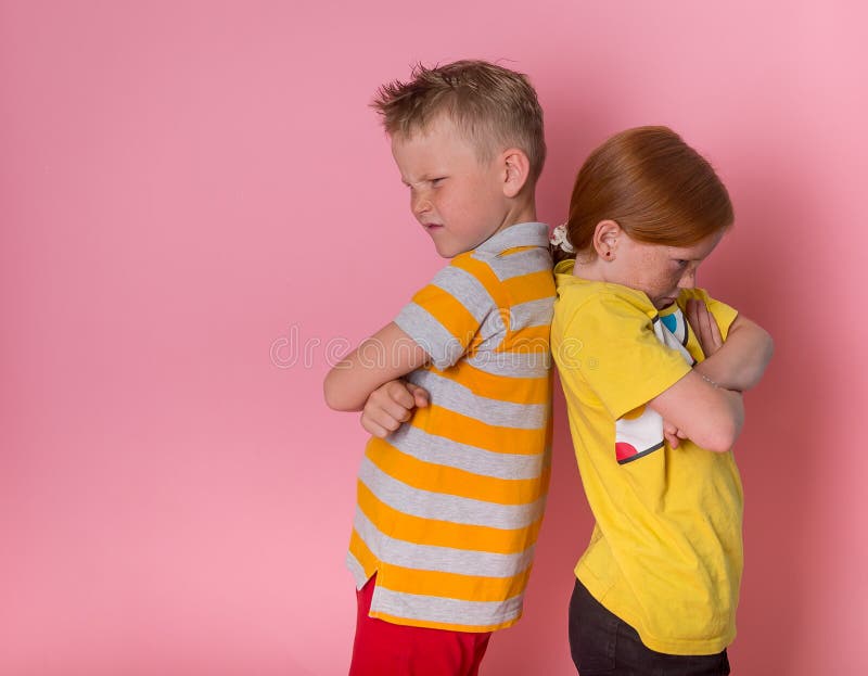 Two angry kids boy and girl. frowning brother and sister standing back to back. School children do not talking to each