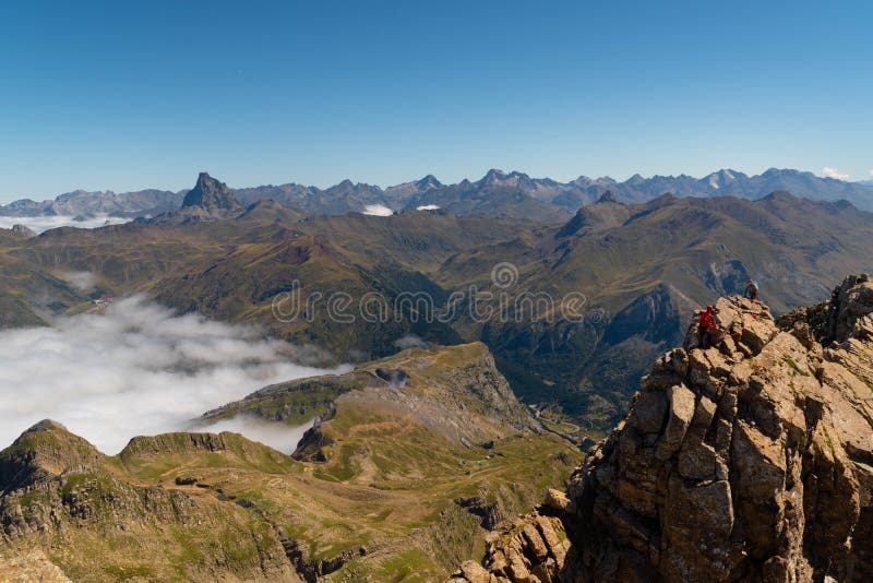 Two anonymous climbers reaching Aspe peak in the Pyrenees with peaks and mountains on the Spanish side and a sea of clouds on the French side in summer season