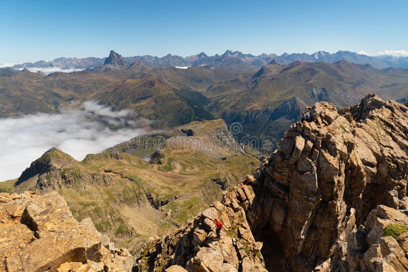 Two anonymous climbers reaching Aspe peak in the Pyrenees with peaks and mountains on the Spanish side and a sea of clouds on the French side in summer season