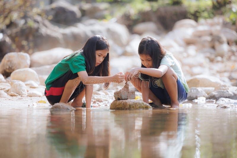 Two asian siblings playing sand nearing the river together with fun.