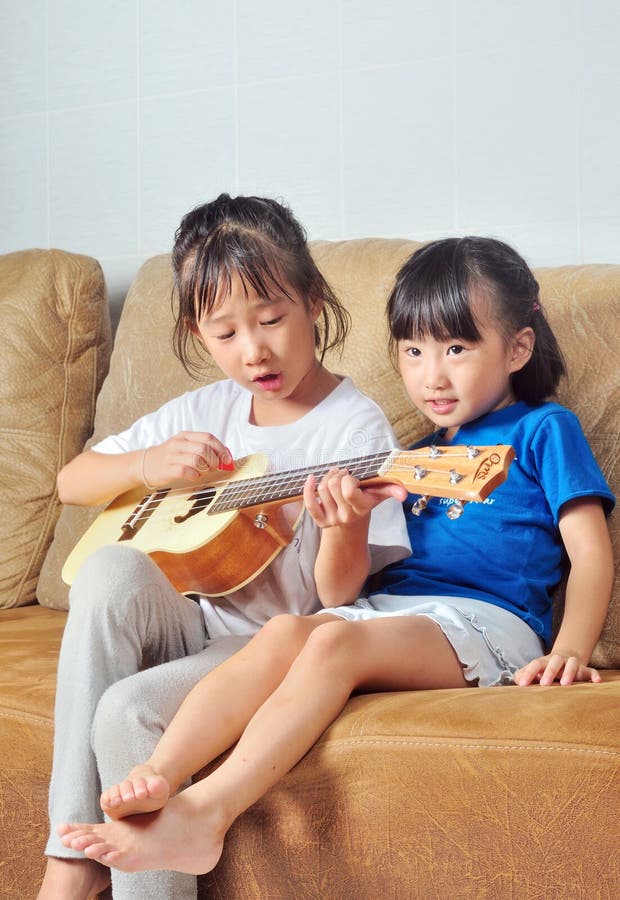 Two asian small girls playing ukulele and singing music together