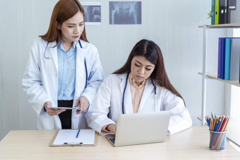 Two Asian Women Doctors Discuss Meeting Doctor`s Office Medical Clinic Using Laptop Consulting