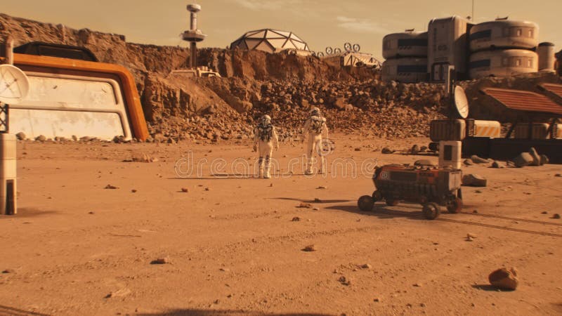 Two astronauts walk on Mars surface near scientific base stock photography
