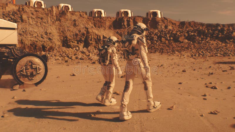 Two astronauts walk toward scientific base on Mars stock photos