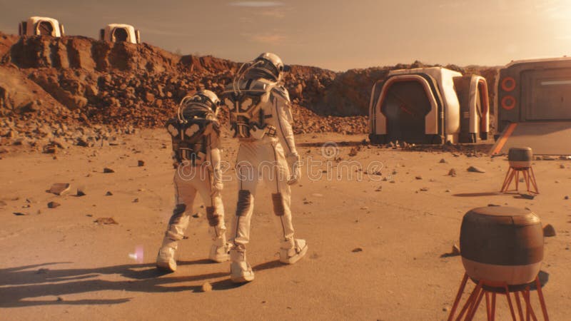 Two astronauts walk toward scientific base on Mars stock photos
