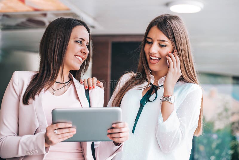 Two attractive young women looking at the tablet screen together and talking on mobile phone stock photo Two attractive young women looking at the tablet screen together and talking on mobile phone stock photo