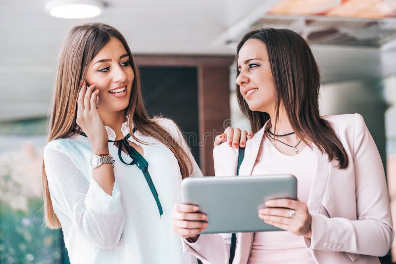 Two attractive young women sharing ideas on a digital tablet and talking on mobile phone royalty free stock photo Two attractive young women sharing ideas on a digital tablet and talking on mobile phone royalty free stock photo