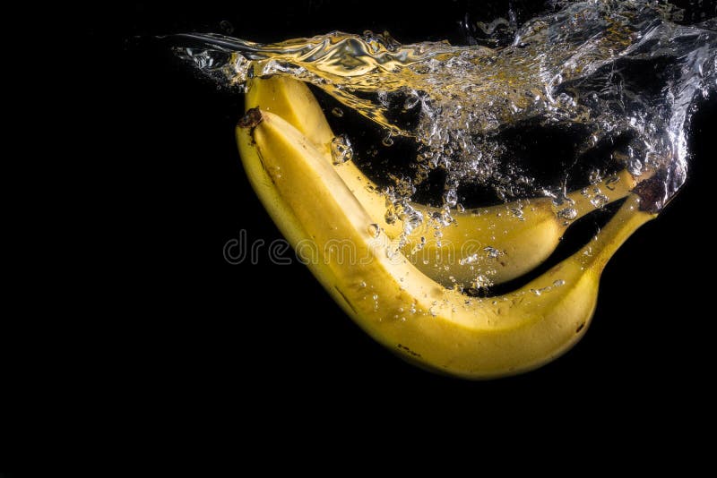 Two Bananas Fall into the Water with Splashes and Bubbles on a Black Background Stock Image