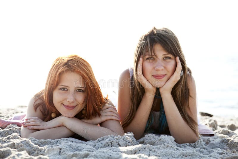 Two beautiful girls lie on the beach.