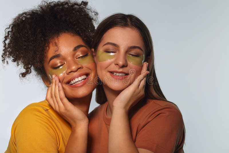 Two beautiful girls posing close to each other cheek to cheek, with applied under eye gel pads