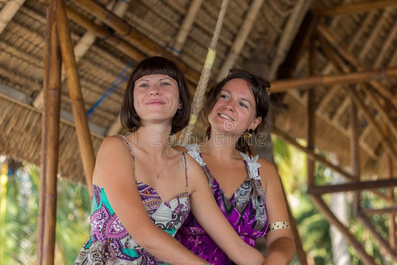 Two Beautiful happy young girls sitting in a wooden gazebo at sunny day. and having fun, smiling and laughing. Tropical