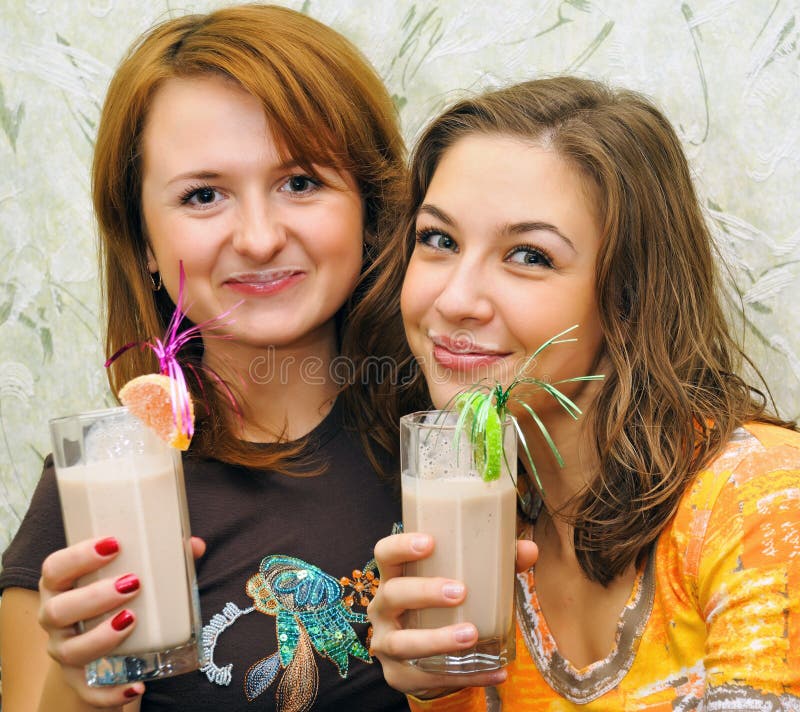 Two beautiful laughing girls drink cocktails