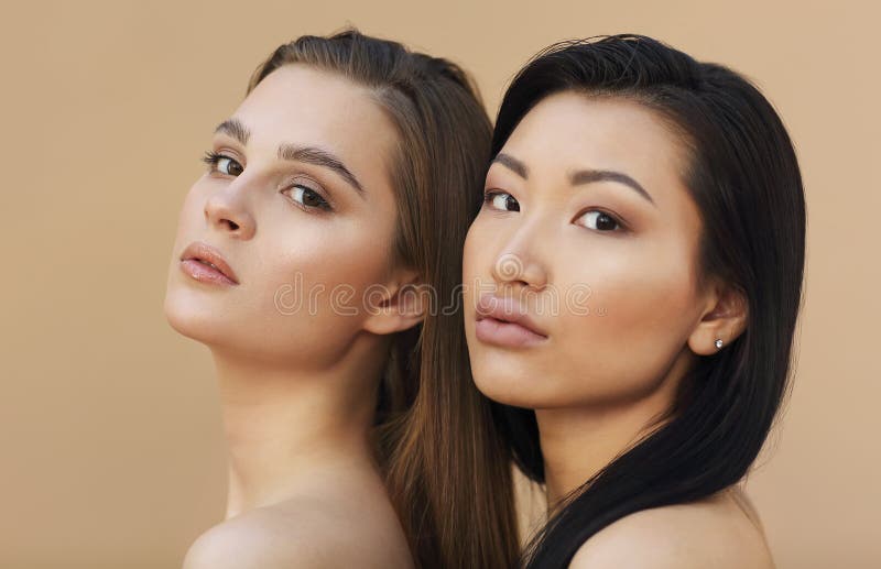 Two beautiful multicultural young women hugging while posing camera