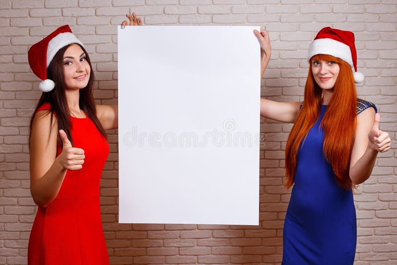 Two beautiful smiling women in Santa caps with thumb up gesture