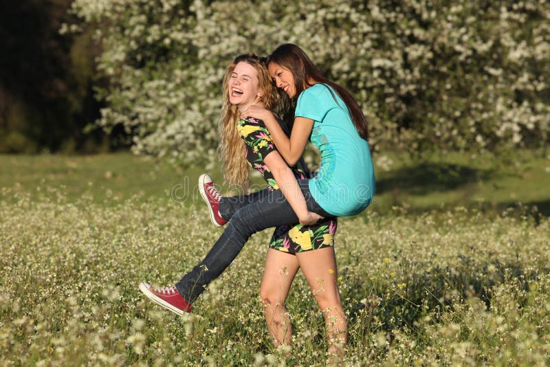 Two beautiful young women piggy- backing in meadow