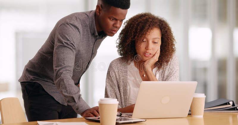 Two black business people working on a laptop while drinking coffee in an office stock photo Two black business people working on a laptop while drinking coffee in an office stock photo