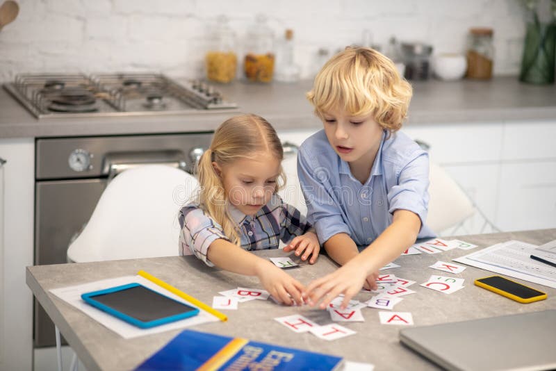 Two blond kids playing with letter cards and looking interested. Smart kids. Two blond kids playing with letter cards and looking interested stock images Two blond kids playing with letter cards and looking interested. Smart kids. Two blond kids playing with letter cards and looking interested stock images
