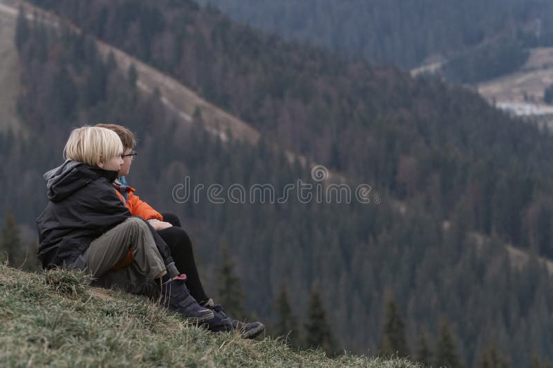 Two boys are sitting on hillside. Portrait of children in autumn in the mountains. Weekend in nature outside