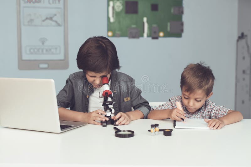 Two boys are sitting at the table. One of them is sitting in front of a gray laptop. They work at the table stock photo Two boys are sitting at the table. One of them is sitting in front of a gray laptop. They work at the table stock photo