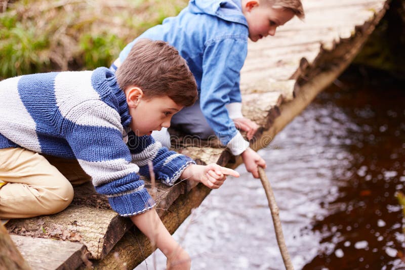 Two Boys On Wooden Bridge Playing With Sticks In Stream