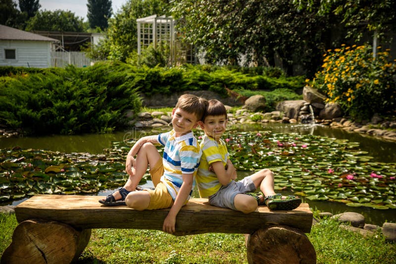 Two brother boys sitting on a bench in a park near peaceful lake