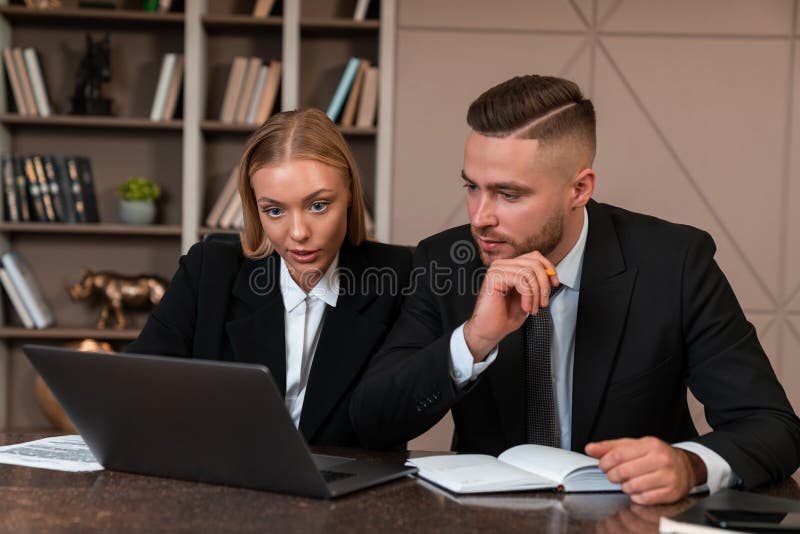 Two business people working together, thoughtful looking at laptop stock photography