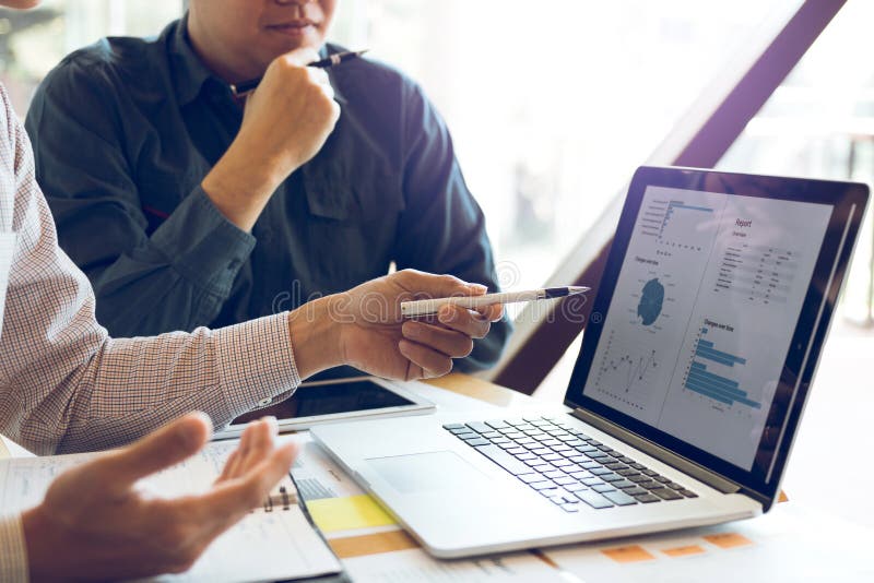 Two businessmen are together analyzing the financial data graph and pointing to the laptop computer screen