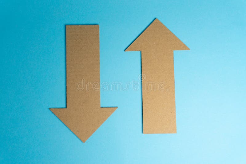 Cardboard cutouts shaped like arrows are arranged on a blue surface. One arrow points up while the other points down. This setup is suitable for design or art projects. Cardboard color shapes stock images, royalty-free photos and pictures