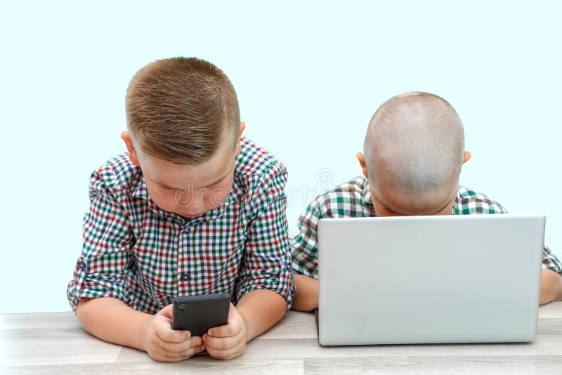 Two Caucasian boys ,brothers on a white isolated background. one plays in the phone,the other in the laptop. modern children and royalty free stock image Two Caucasian boys ,brothers on a white isolated background. one plays in the phone,the other in the laptop. modern children and royalty free stock image