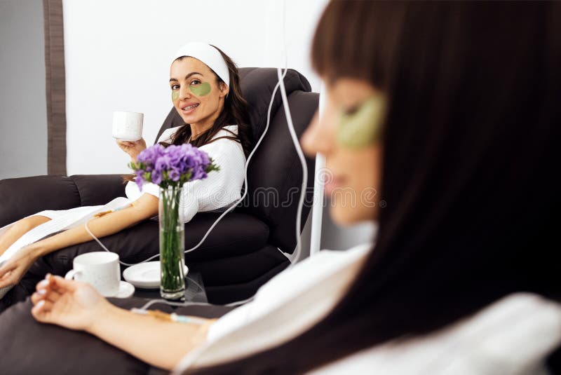 Two caucasian girls in bathrobes make wellness dropper with vitamins in a beauty salon. IV vitamin therapy