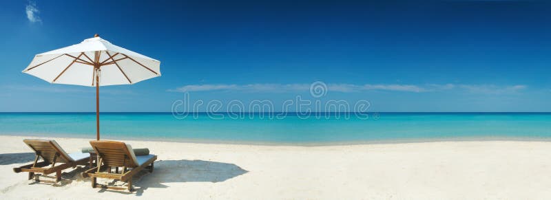 Panorama-Blick auf zwei Stühlen und weißen Sonnenschirm am Strand.