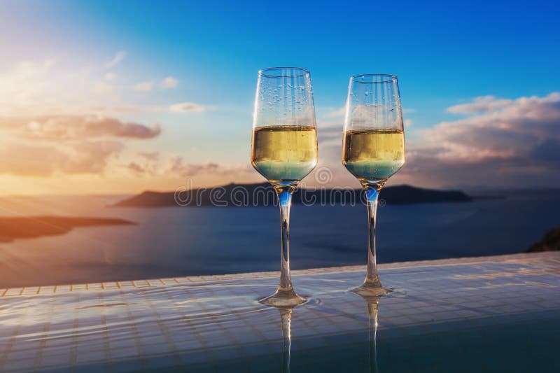 Two champagne glasses on the edge of infinity swimming pool at sunset on Santorini island