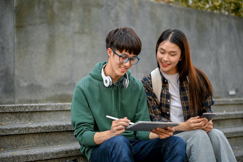 Two cheerful Asian college students using tablet on campus building outdoor stairs