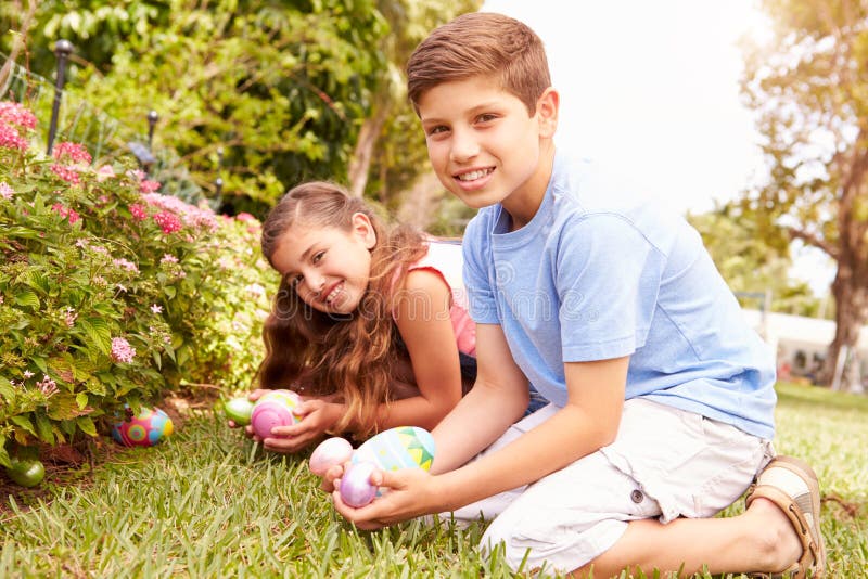Two Children Having Easter Egg Hunt In Garden