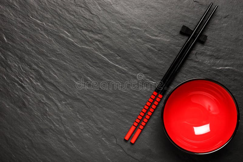 Two chopsticks and red plate on black stone background