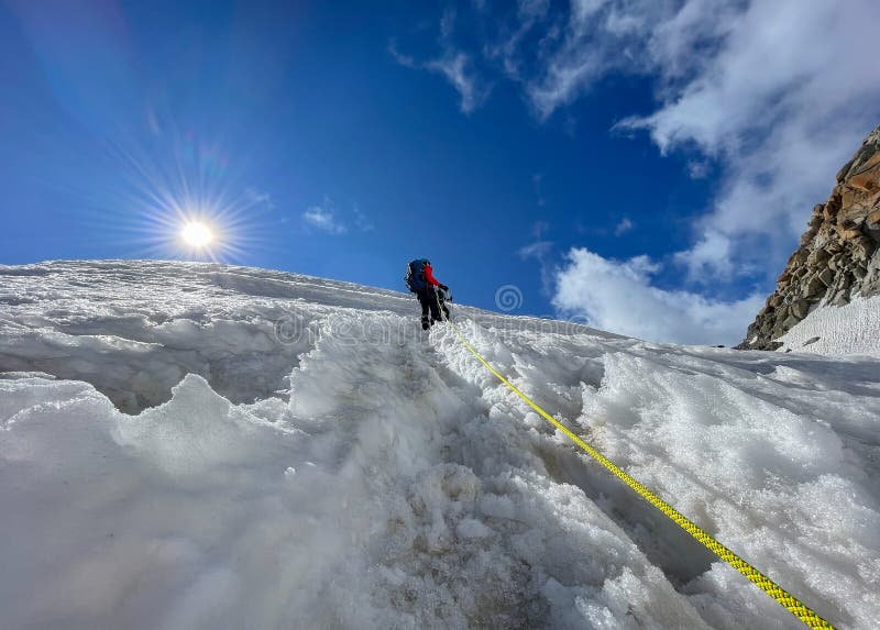 Two climbers climbing uphill on snowy slope as rope team on sunny day under Mont Blanc du Tacul mount 4248m, French Alps, France. Sports, climbing, mountaineering concept