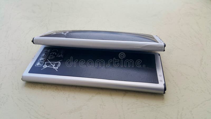 Two close-up batteries, one regular and the other a swollen lithium-ion smartphone battery. A damaged battery is ready to burn or royalty free stock image