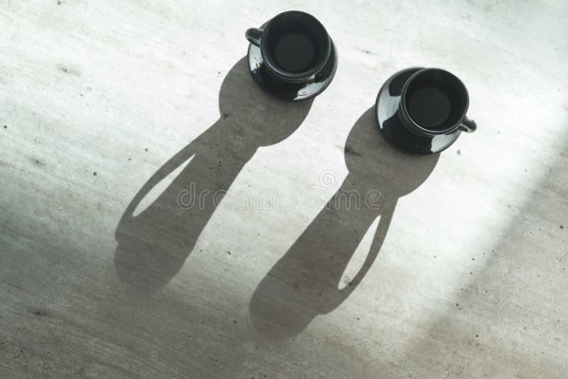 Two Coffee clay black cups on table with bright backlight which draws long cup shadows. Coffee for couple in modern kitchen stock photo Two Coffee clay black cups on table with bright backlight which draws long cup shadows. Coffee for couple in modern kitchen stock photo