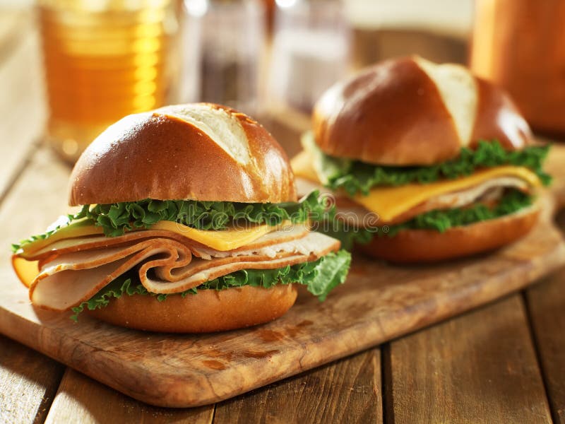 Two cold cut style turkey and cheese sandwiches on pretzel buns