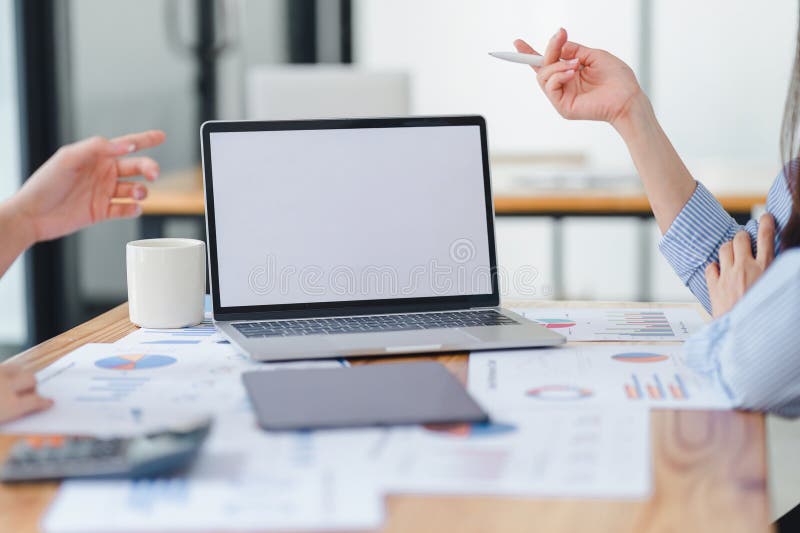 Two colleagues discussing business data with blank screen laptop and charts on the table, focusing on teamwork and data royalty free stock photos