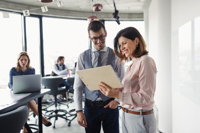 Two collegues talking about project document, standing in modern office. stock photo