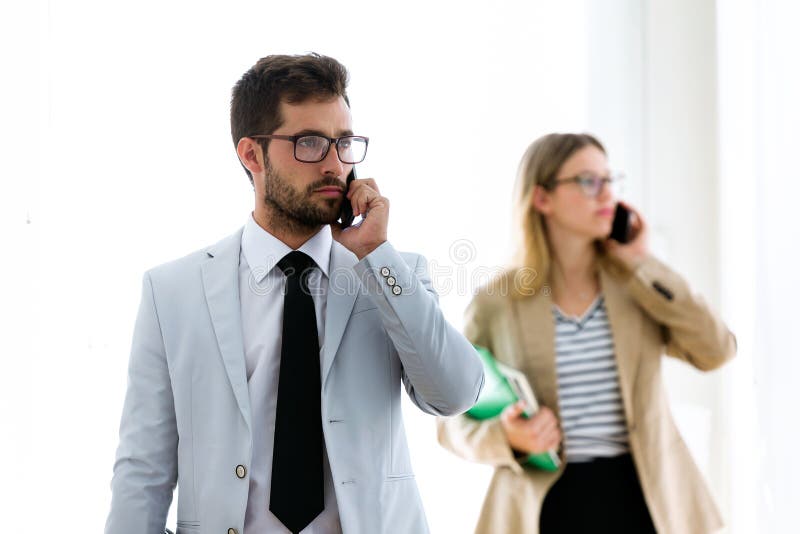 Two concentrated young business partners talking with their smartphones in a hallway of they company.