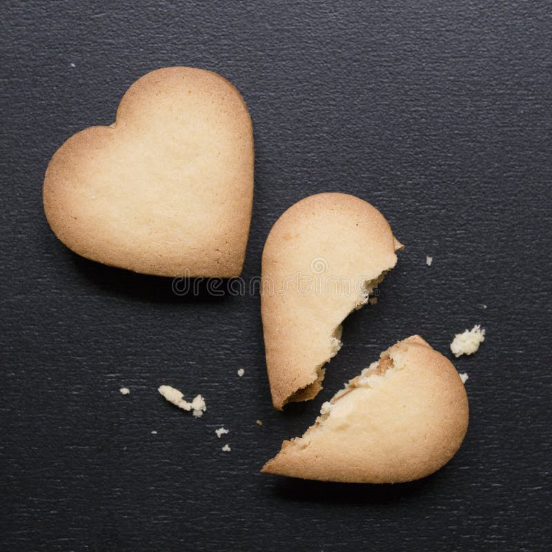 Two cookies in the shape of heart, one of them is broken on black background. Cracked heart shaped cookie as concept of breakup royalty free stock images Two cookies in the shape of heart, one of them is broken on black background. Cracked heart shaped cookie as concept of breakup royalty free stock images