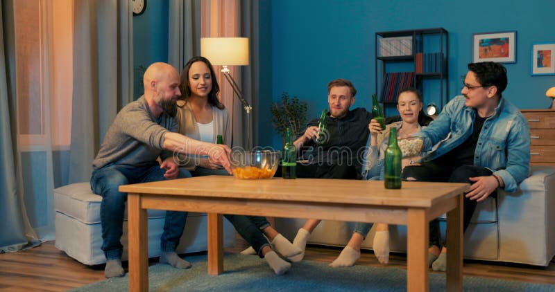 Two couples in love and one single, sitting on couch in evening, spending time together stock video footage