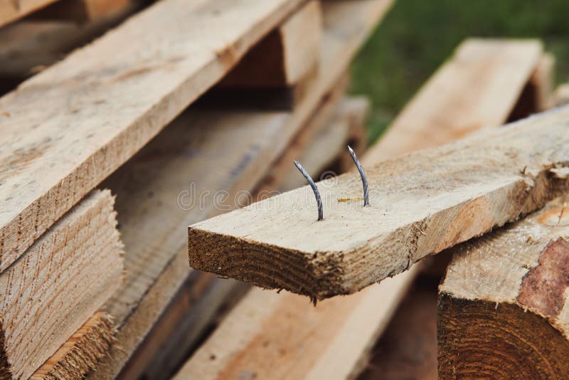 Two crooked sharp nails sticking out of the wooden board.