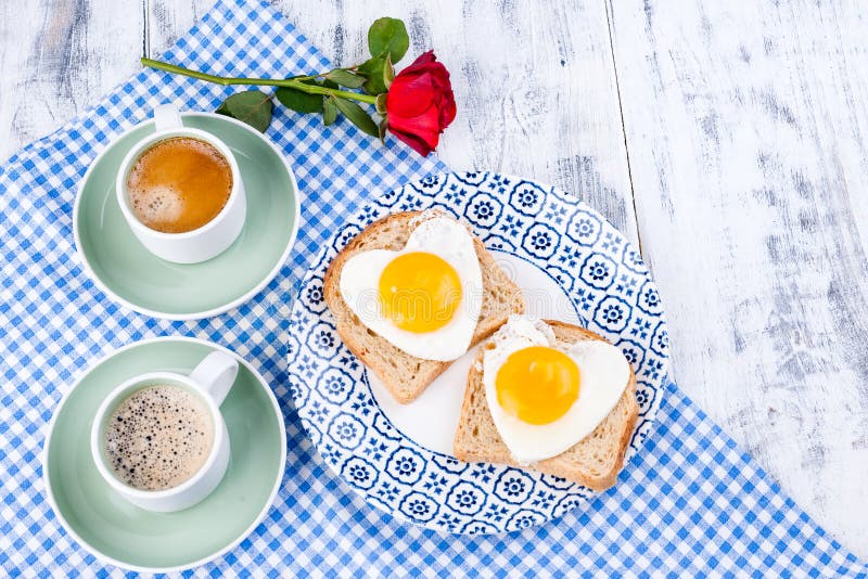 Two cups of aromatic coffee and heart-shaped toasts for a romantic morning of lovers. Red rose and morning surprise for breakfast