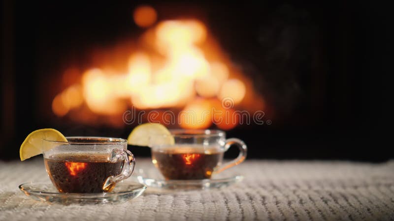 Two cups of hot tea with lemon on a table against the background of the fireplace. Hot cafe video