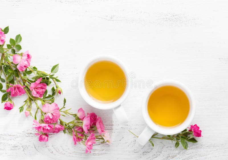 Two cups of tea and branch of small pink roses. stock photos